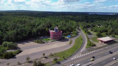 Bulutlu bir günde çevresi ormanla çevrili bir otoyolda giden arabalar göle çıkıyor. İHA yükseliyor 