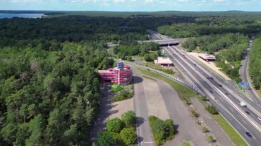 Bulutlu bir günde çevresi ormanla çevrili bir otoyolda giden arabalar göle çıkıyor. panorama yörünge dronu 