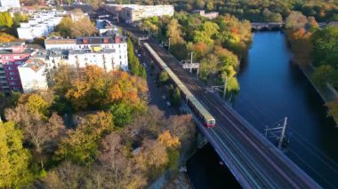 Berlin 'de bir köprüyü geçen trenin manzarası. Etrafı canlı sonbahar yapraklarıyla çevrili. İHA kamerası aşağıya bakıyor 
