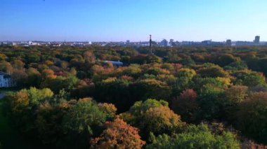 Tiergarten Park 'ın canlı sonbahar yeşillikleri üzerinde yükselen ikonik Berlin zafer sütununun havadan görünüşü. Arka planda şehir manzarası var. doly sağ drone 