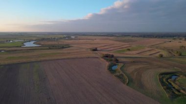 Üretilmiş tarlaları, uzak bir nehir ve ormanı olan verimli bir ovanın havadan görünüşü batan güneşin sıcacık ışığında yıkanmıştı. panorama genel görünüm dronu 