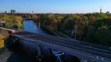 Berlin 'de bir köprüyü geçen trenin manzarası. Etrafı canlı sonbahar yapraklarıyla çevrili. Ters İHA uçuşu 