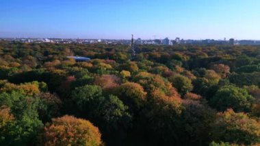 Tiergarten Park 'ın canlı sonbahar yeşillikleri üzerinde yükselen ikonik Berlin zafer sütununun havadan görünüşü. Arka planda şehir manzarası var. Ters İHA uçuşu 