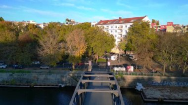 Güneşli bir günde Berlin 'in manzara manzarası... bir kanalı, bir köprüyü, binaları ve renkli sonbahar ağaçlarını içeriyor. Yukarıdan aşağıya uçan vinç drone 'u 