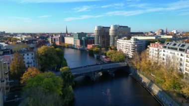 Güneşli bir günde Berlin 'in manzara manzarası... bir kanalı, bir köprüyü, binaları ve renkli sonbahar ağaçlarını içeriyor. uçuş üstü insansız hava aracı 