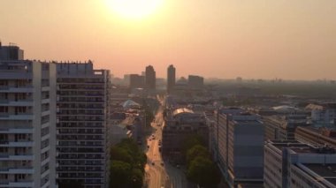 Gün batımında bir bulvarda giden arabalar, ağaçlarla ve apartmanlarla dolu bir şehir manzarasında. İHA alçalıyor 