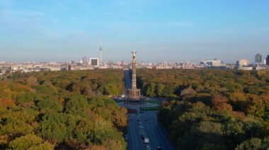 Renkli sonbahar yapraklarıyla çevrili ikonik bir dönüm noktası, açık mavi gökyüzünün altında Berlin şehri manzarası. panorama genel görünüm dronu 