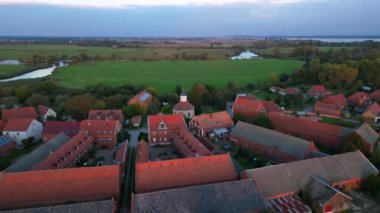 Altın saat ışığıyla aydınlatılan küçük bir köyün havadan görünüşü, etrafındaki tarlaların üzerine uzun gölgeler düşürüyor. Yukarıdan insansız hava aracı görüntüleri 
