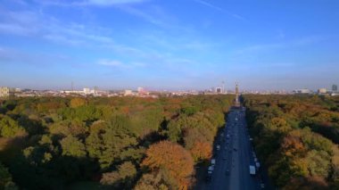 Renkli sonbahar yapraklarıyla çevrili ikonik bir dönüm noktası, açık mavi gökyüzünün altında Berlin şehri manzarası. Dolly sol İHA 