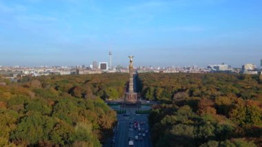 Renkli sonbahar yapraklarıyla çevrili ikonik bir dönüm noktası, açık mavi gökyüzünün altında Berlin şehri manzarası. İticileri ileri çalıştır 