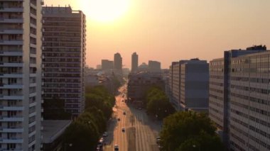 Gün batımında bir bulvarda giden arabalar, ağaçlarla ve apartmanlarla dolu bir şehir manzarasında. İHA yükseliyor 