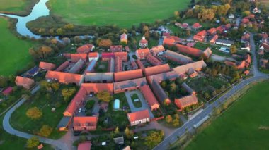 Altın saat ışığıyla aydınlatılan küçük bir köyün havadan görünüşü, etrafındaki tarlaların üzerine uzun gölgeler düşürüyor. Yukarıdan insansız hava aracı görüntüleri 