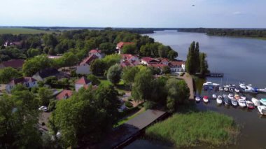 Huzurlu bir gölün kıyısındaki sakin bir köyün yakınındaki sakin bir limana demirlemiş teknelerin hava manzarası, yeşillikle çevrili. panorama genel görünüm dronu 