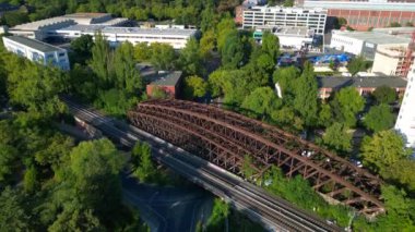 Berlin 'deki Liesenbrucke Köprüsü' nün havadan görünüşü demiryolu raylarını, duvar yazılarını, ağaçları ve çevresindeki kentsel manzarayı gösteriyor. İHA alçalıyor 