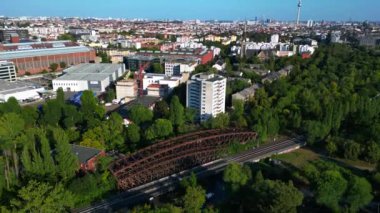 Berlin 'deki yemyeşil şehir merkezinde tren raylarının üzerinden geçen paslı demiryolu köprüsü, ulaşım altyapısı ve kentsel yeşillik entegrasyonu. İHA alçalıyor 