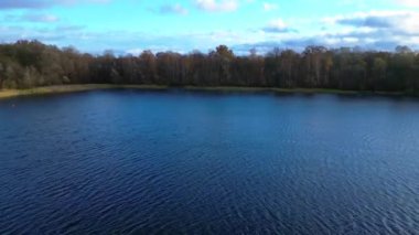 İnsansız hava aracı, parçalı bulutlu gökyüzünün altında sakin gölü çevreleyen renkli ormanın nefes kesici manzarasını yakalıyor. uçuş üstü insansız hava aracı 