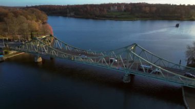 Berlin, Almanya 'da güneşli bir sonbahar gününde arabalı Glienicke Köprüsü ve Havel Nehri' ni geçen bir tur teknesi. panorama yörünge dronu 