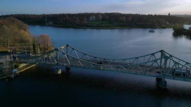 Berlin, Almanya 'da güneşli bir sonbahar gününde arabalı Glienicke Köprüsü ve Havel Nehri' ni geçen bir tur teknesi. Ters İHA uçuşu 