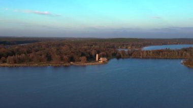 Sacrow limanında renkli sonbahar yeşillikleri ve Kurtarıcı Kilisesi ile çevrili sakin mavi bir göl manzarası. panorama yörünge dronu 