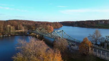 Havel nehrinin üzerindeki glienicke köprüsünün renkli bir sonbahar günbatımında üzerinde arabalar geziniyor. panorama yörünge dronu 