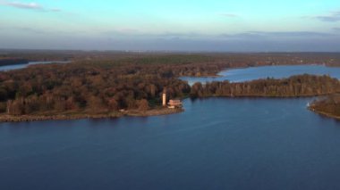 Sacrow limanında renkli sonbahar yeşillikleri ve Kurtarıcı Kilisesi ile çevrili sakin mavi bir göl manzarası. panorama yörünge dronu 