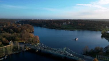 Berlin, Almanya 'da güneşli bir sonbahar gününde arabalı Glienicke Köprüsü ve Havel Nehri' ni geçen bir tur teknesi. İHA alçalıyor 