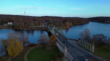 Havel nehrinin üzerindeki glienicke köprüsünün renkli bir sonbahar günbatımında üzerinde arabalar geziniyor. panorama yörünge dronu 
