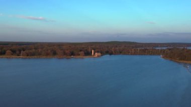 Sacrow limanında renkli sonbahar yeşillikleri ve Kurtarıcı Kilisesi ile çevrili sakin mavi bir göl manzarası. İticileri ileri çalıştır 