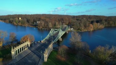 Havel nehrinin üzerindeki glienicke köprüsünün renkli bir sonbahar günbatımında üzerinde arabalar geziniyor. panorama yörünge dronu 