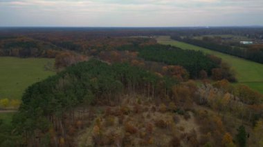 Yukarıdan görülen yeşil bir tarlanın çevresindeki canlı bir sonbahar ormanından geçen demiryolu rayları. Ters İHA uçuşu 