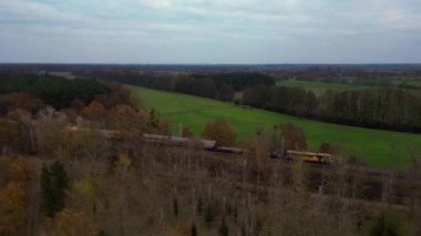 Tren, orman yakınlarındaki yeşil çayırdan geçiyor. Renkli sonbahar ağaçları ve hava manzarası var. Ters İHA uçuşu 