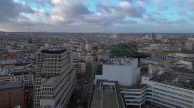 Berlin 'in hava manzarası bulutlu bir gökyüzü altında modern ve tarihi binaları, sokakları ve kentsel yoğunluğu gösteriyor. Yukarıdan aşağıya doğru uçur 