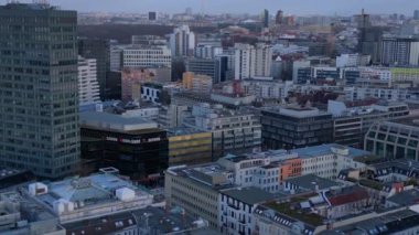 Berlin 'in hava manzarası bulutlu bir gökyüzü altında modern ve tarihi binaları, sokakları ve kentsel yoğunluğu gösteriyor. Drone 'u yukarı eğ 