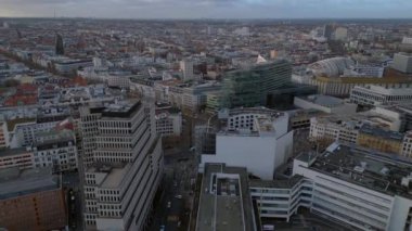 Berlin 'in hava manzarası bulutlu bir gökyüzü altında modern ve tarihi binaları, sokakları ve kentsel yoğunluğu gösteriyor. Yukarıdan insansız hava aracı görüntüleri 