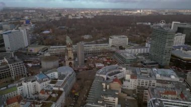 Berlin 'in hava manzarası bulutlu bir gökyüzü altında modern ve tarihi binaları, sokakları ve kentsel yoğunluğu gösteriyor. İHA alçalıyor 