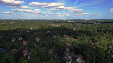 Hayır, Berlin 'de bir yerleşim bölgesi. Yoğun bir ormanın içine yerleştirilmiş evler var. Ufukta şehrin ufku görünüyor. doly sağ drone 