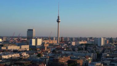 Berlin TV kulesi şehrin üzerinde dikiliyor, altın saatin sıcacık parıltısıyla yıkanıyor. Yukarıdan insansız hava aracı görüntüleri 