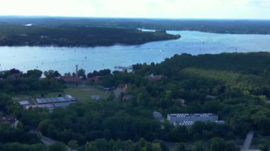 Wannsee göllerinde gezinen yelkenliler, güneşli bir günde, mavi gökyüzü ve bulutlarla çevrili yemyeşil ormanlarla çevrilidir. Sağ drona döndür 
