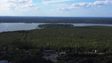 Wannsee göllerinde gezinen yelkenliler, güneşli bir günde, mavi gökyüzü ve bulutlarla çevrili yemyeşil ormanlarla çevrilidir. panorama genel görünüm dronu 