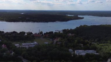 Wannsee göllerinde gezinen yelkenliler, güneşli bir günde, mavi gökyüzü ve bulutlarla çevrili yemyeşil ormanlarla çevrilidir. doly sağ drone 