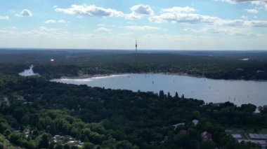 Wannsee göllerinde gezinen yelkenliler, güneşli bir günde, mavi gökyüzü ve bulutlarla çevrili yemyeşil ormanlarla çevrilidir. Sağ drona döndür 