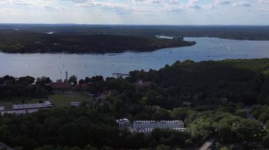 Wannsee göllerinde gezinen yelkenliler, güneşli bir günde, mavi gökyüzü ve bulutlarla çevrili yemyeşil ormanlarla çevrilidir. Dolly sol İHA 