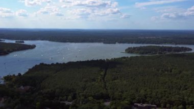 Wannsee göllerinde gezinen yelkenliler, güneşli bir günde, mavi gökyüzü ve bulutlarla çevrili yemyeşil ormanlarla çevrilidir. panorama genel görünüm dronu 