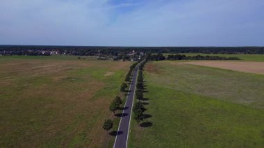 Ağaçlar ve tarlalarla dolu kırsal bir araziden geçen boş bir asfalt yolun havadan görünüşü. Ters İHA uçuşu 