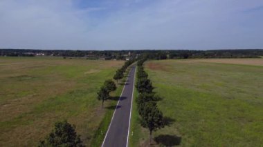 Ağaçlar ve tarlalarla dolu kırsal bir araziden geçen boş bir asfalt yolun havadan görünüşü. Ters İHA uçuşu 