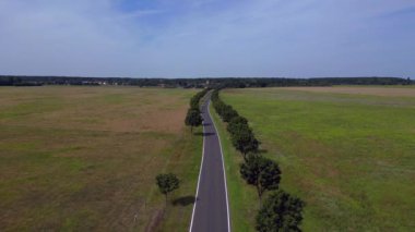 Ağaçlar ve tarlalarla dolu kırsal bir araziden geçen boş bir asfalt yolun havadan görünüşü. İHA 'yı çek 