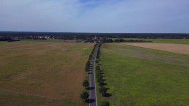 Ağaçlar ve tarlalarla dolu kırsal bir araziden geçen boş bir asfalt yolun havadan görünüşü. Ters İHA uçuşu 