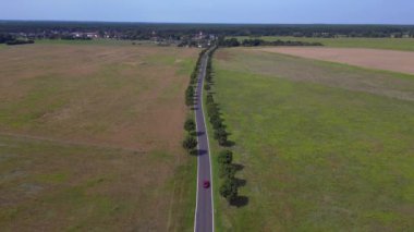 Asfalt bir yolda, ağaçlar ve tarlalarla dolu kırsal bir araziden geçen bir arabanın hava görüntüsü. panorama genel görünüm dronu 
