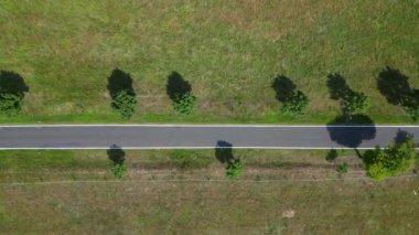 Kırsal bir yolda mavi gökyüzünün altındaki geniş tarlalardan geçen arabaların hava görüntüsü. Yukarıdan aşağıya doğru uçur 