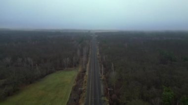 Demiryolu manzarası bulutlu gökyüzü altındaki büyük ormanı geçerek karamsar ve atmosferik manzaralar yaratıyor. Ters İHA uçuşu 